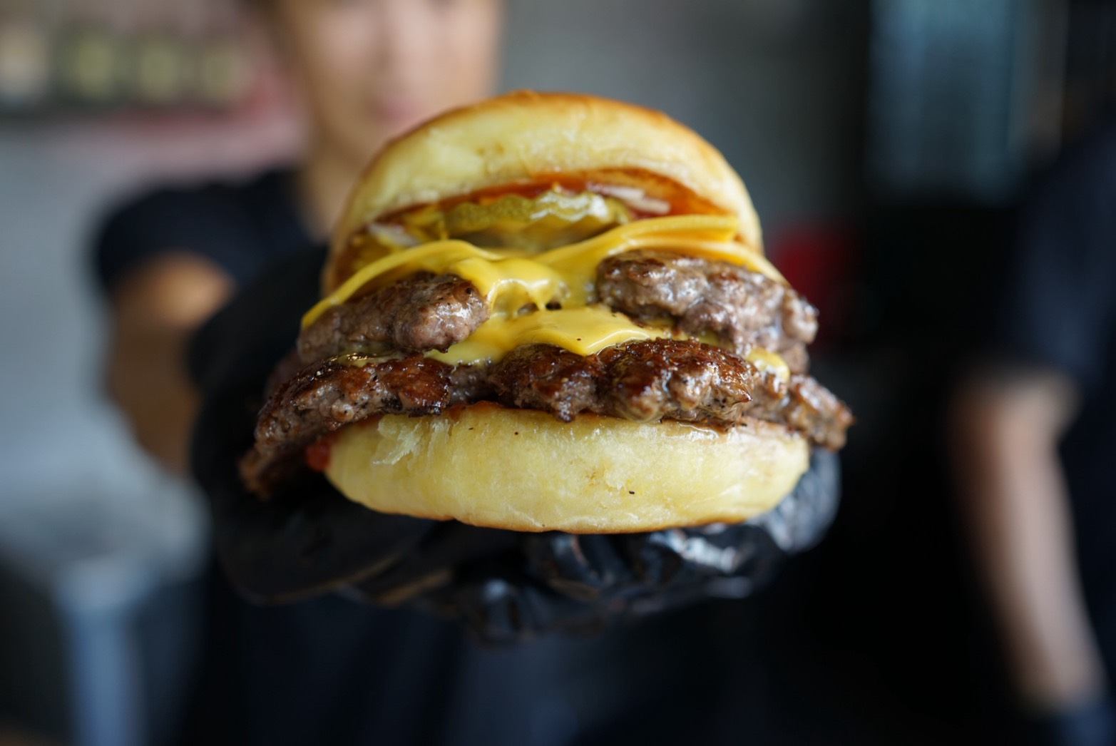 Double smashburger with melting cheese held up in gloved hands at Homies Burger and Fries, Koh Samui
