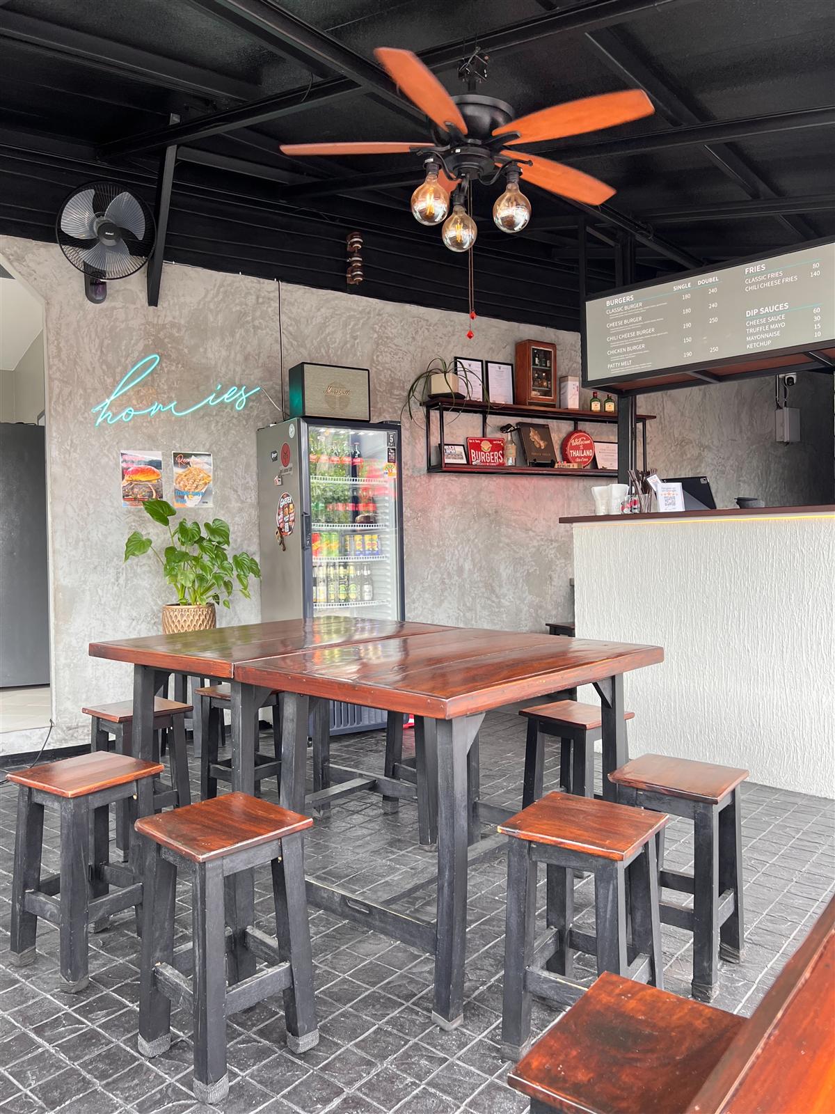 Inside Homies Burger and Fries — teal neon sign, concrete walls, wooden tables and the menu board above the counter