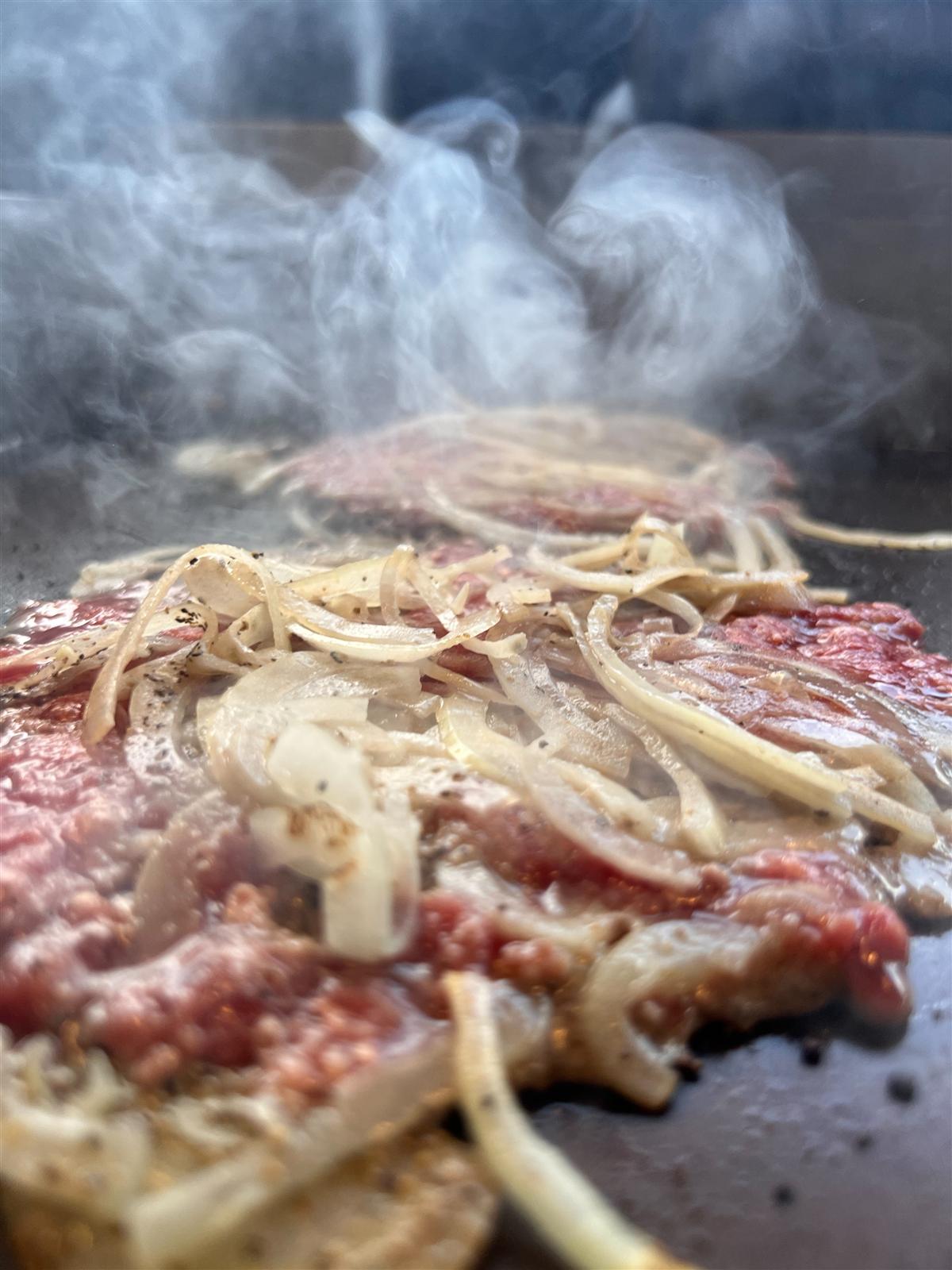 Smashburger patties with onions smoking on a hot griddle